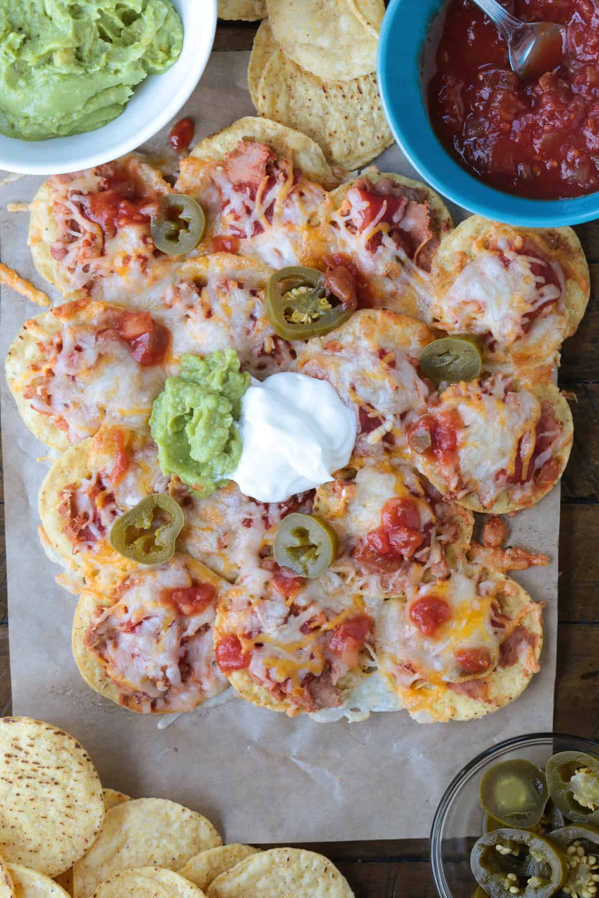 Air Fryer Nachos are so easy to make your kids can do it on their own. Ready in just 5 minutes for after school snacks, appetizers or dinner! nachos on parchment with toppings on the side