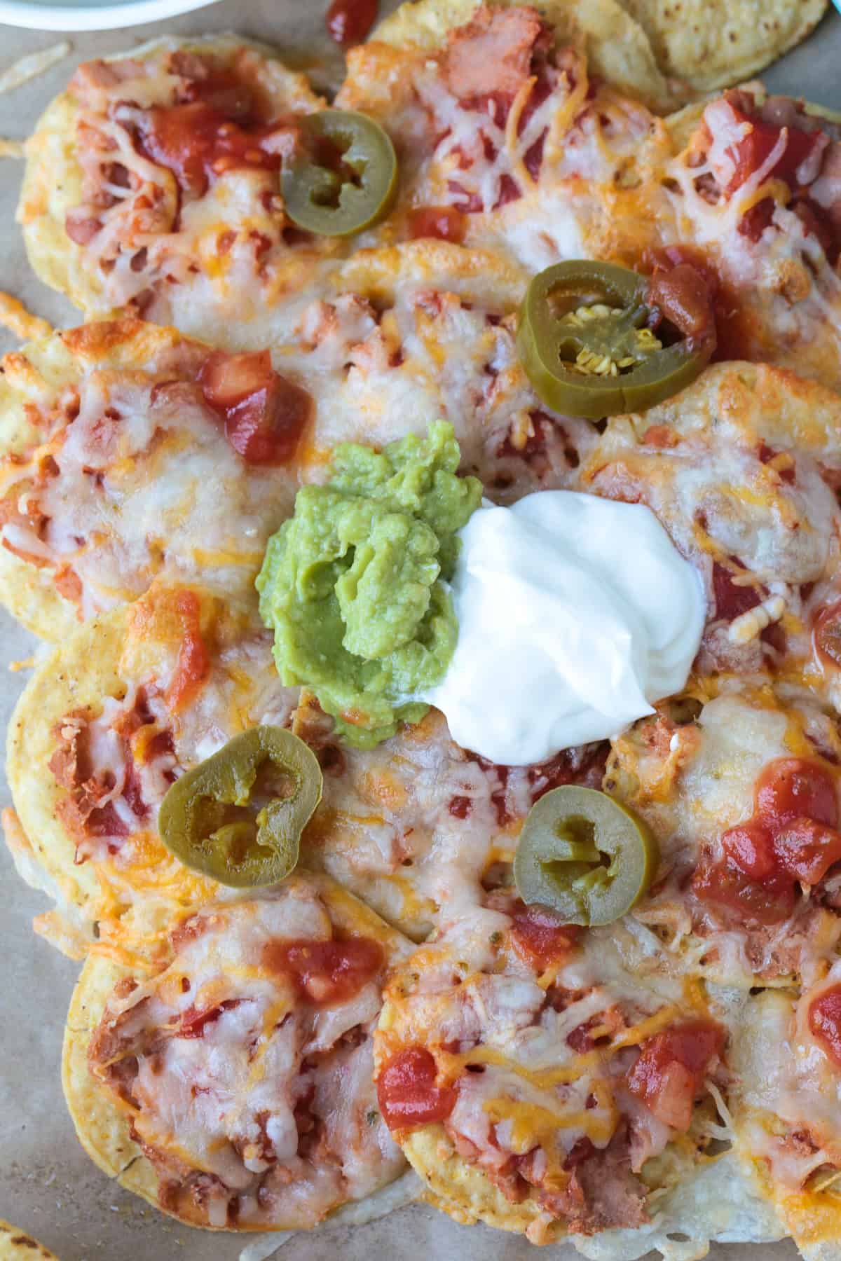 Air Fryer Nachos are so easy to make your kids can do it on their own. Ready in just 5 minutes for after school snacks, appetizers or dinner! nachos on parchment with guacamole and sour cream