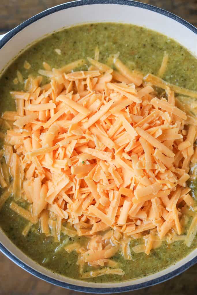 broccoli soup in pot with shredded cheddar cheese