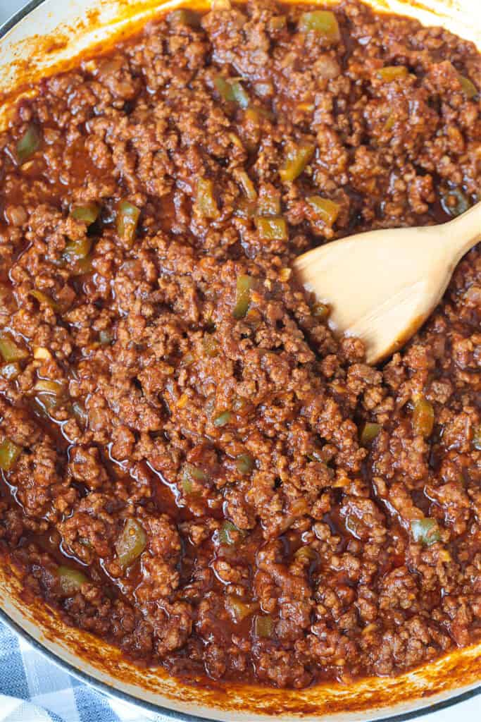 The best Homemade Sloppy Joes! Ground beef in a sweet and tangy sauce with green pepper and sweet onion. Ready in less than 30 minutes! sloppy joe meat in a skillet with wooden spoon