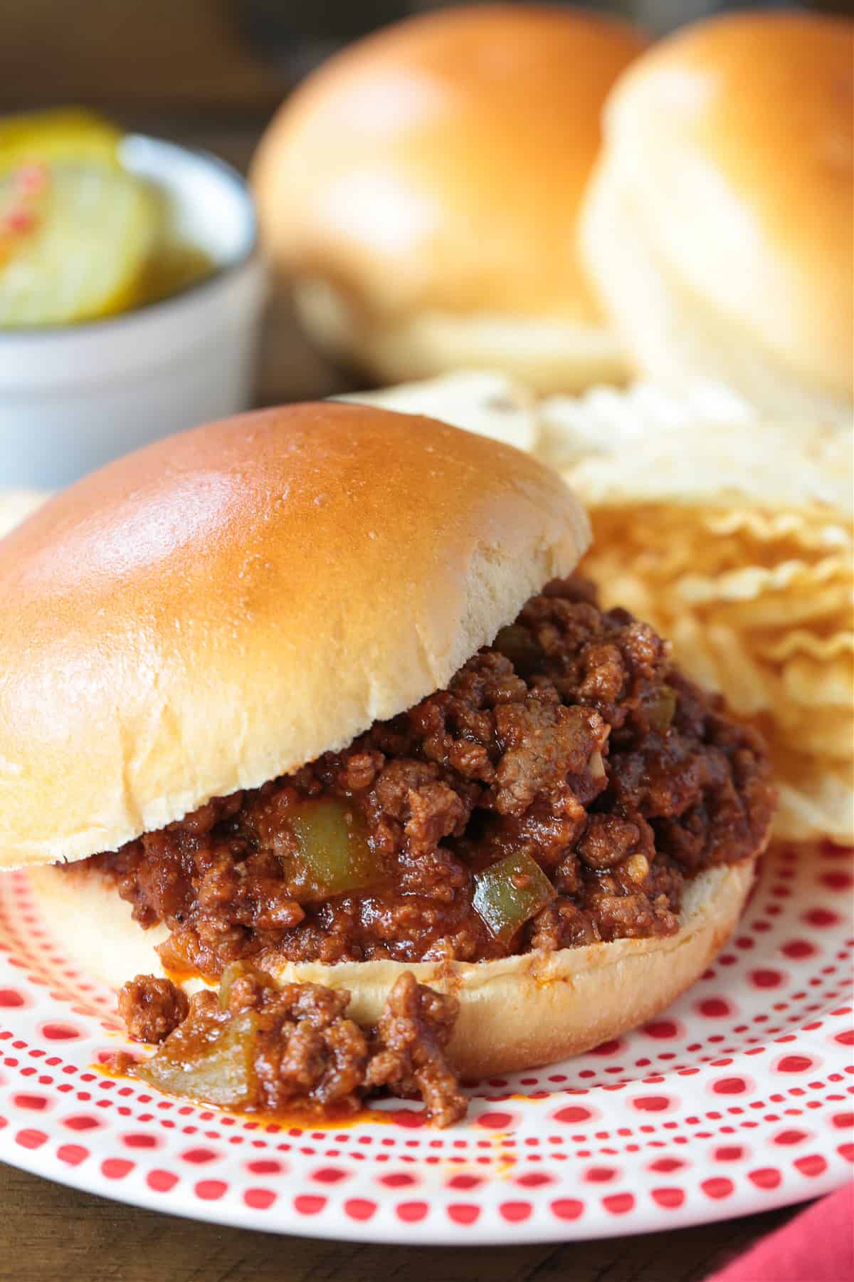The best Homemade Sloppy Joes! Ground beef in a sweet and tangy sauce with green pepper and sweet onion. Ready in less than 30 minutes! sloppy joe sandwich in red and white plater with chips