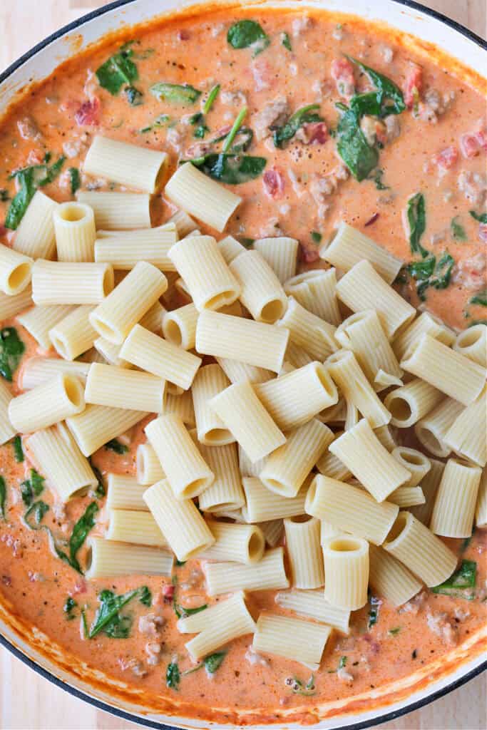 This creamy Pasta with Sausage and Spinach is sure to hit the spot! An easy to make pasta recipe that's ready to serve in just 30 minutes. rigatoni in a skillet with pink cream sauce