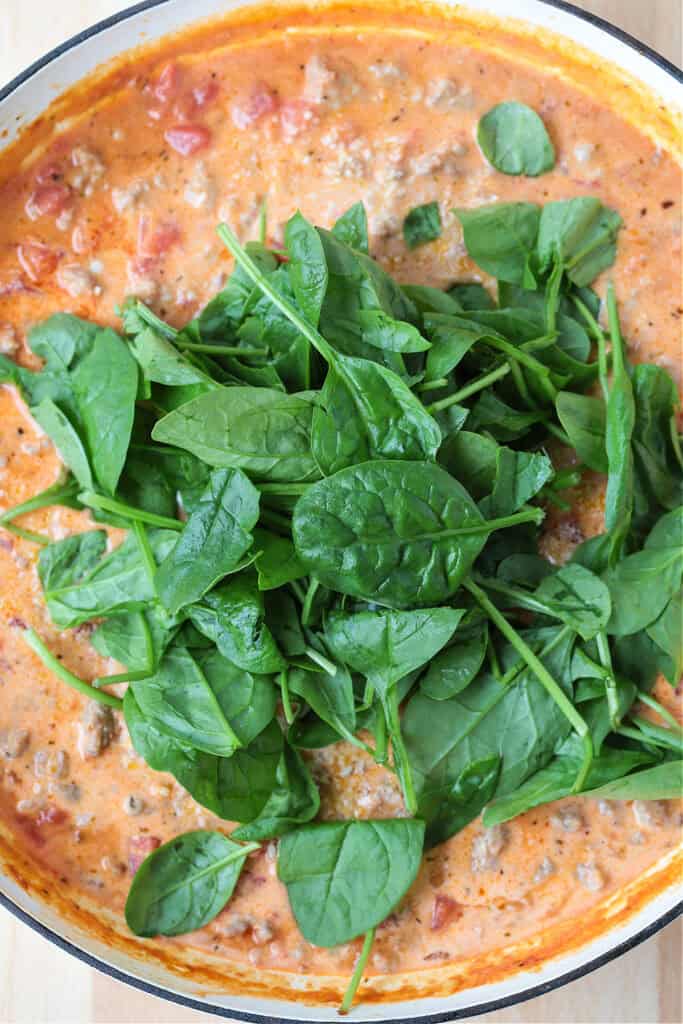 This creamy Pasta with Sausage and Spinach is sure to hit the spot! An easy to make pasta recipe that's ready to serve in just 30 minutes. fresh spinach in a skillet with cream sauce