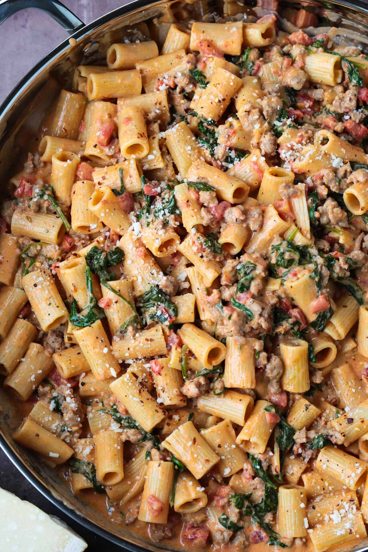 This creamy Pasta with Sausage and Spinach is sure to hit the spot! An easy to make pasta recipe that's ready to serve in just 30 minutes. pasta with sausage in a pink cream sauce in large skillet