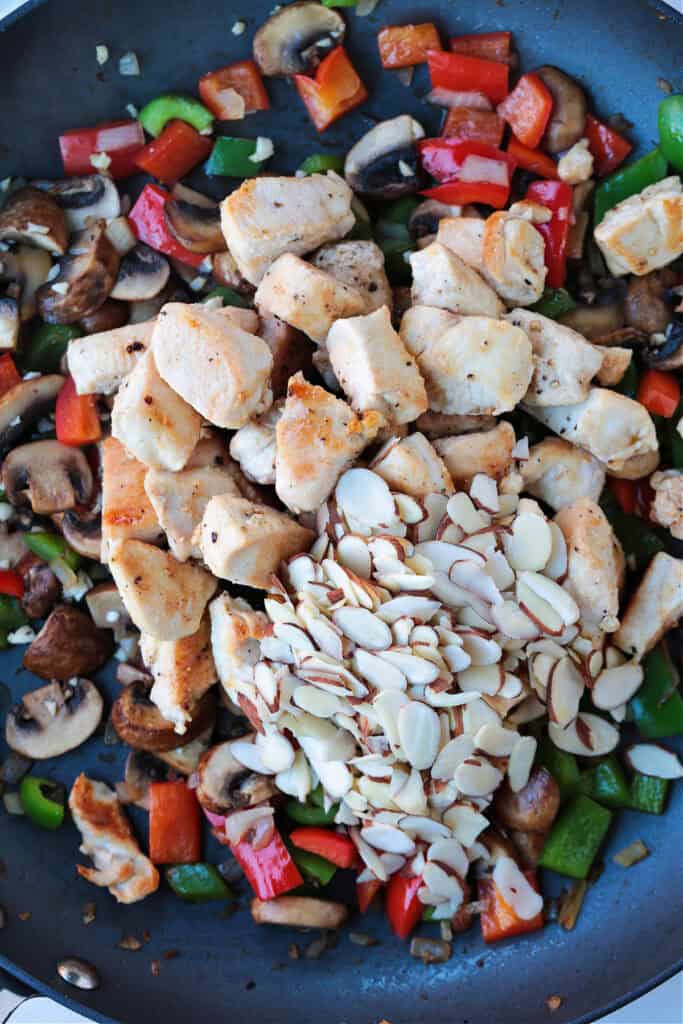 This Almond Chicken recipe is so easy to make and so delicious! Tossed with out homemade 5 minute stir fry sauce, it's better than take out! chicken and sliced almonds in a skillet with vegetables