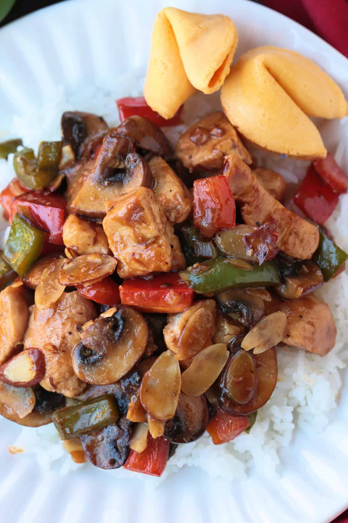 This Almond Chicken recipe is so easy to make and so delicious! Tossed with out homemade 5 minute stir fry sauce, it's better than take out! almond chicken on white plate with rice and fortune cookies