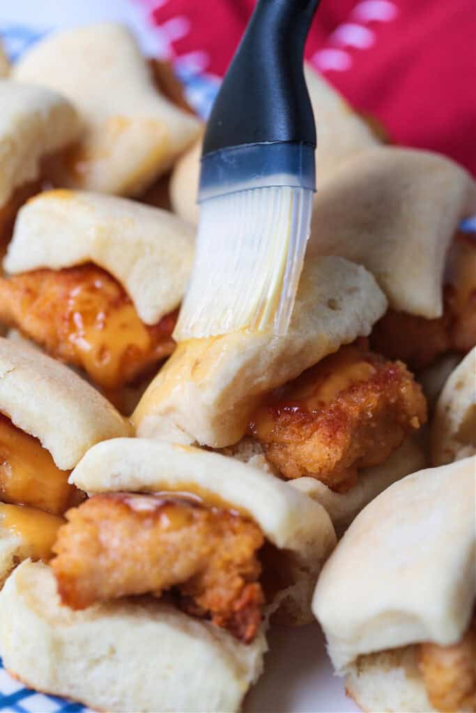 Make these Copycat Chicken Minis for your next party or game day! Just like the Chick Fil A version only better because they're homemade! brushing butter on top of slider roll