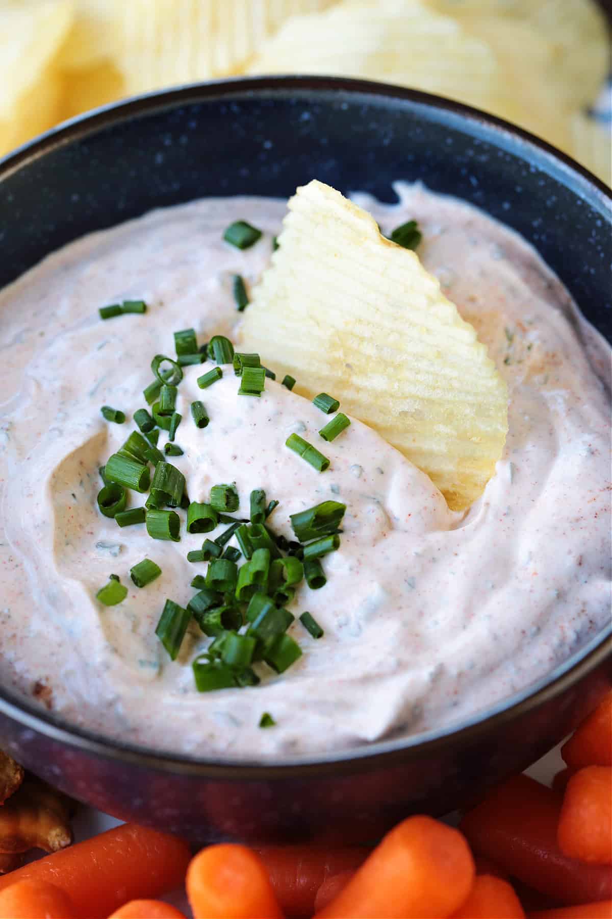 This Sour Cream Dip is a party appetizer staple! Perfect for dipping chips, pretzels and veggies, everyone will be asking for the recipe! potato chip dipping into bowl of dip