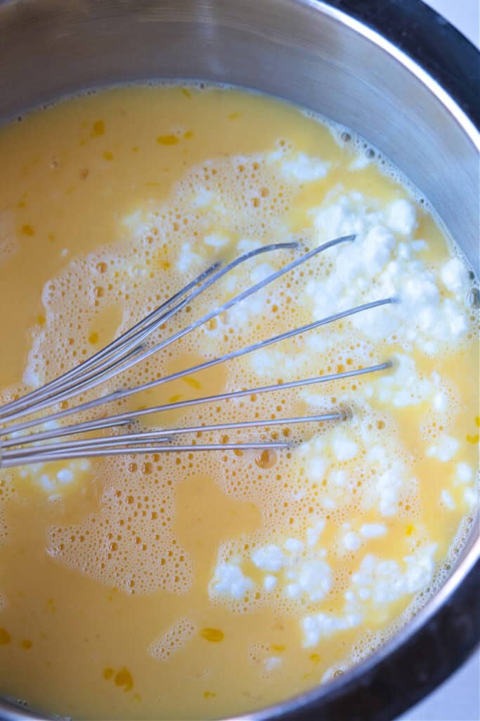 This Italian Breakfast Casserole is delicious for brunch or dinner with a salad! We love this cozy and hearty casserole any time of the day! egg an cottage cheese in bowl with whisk