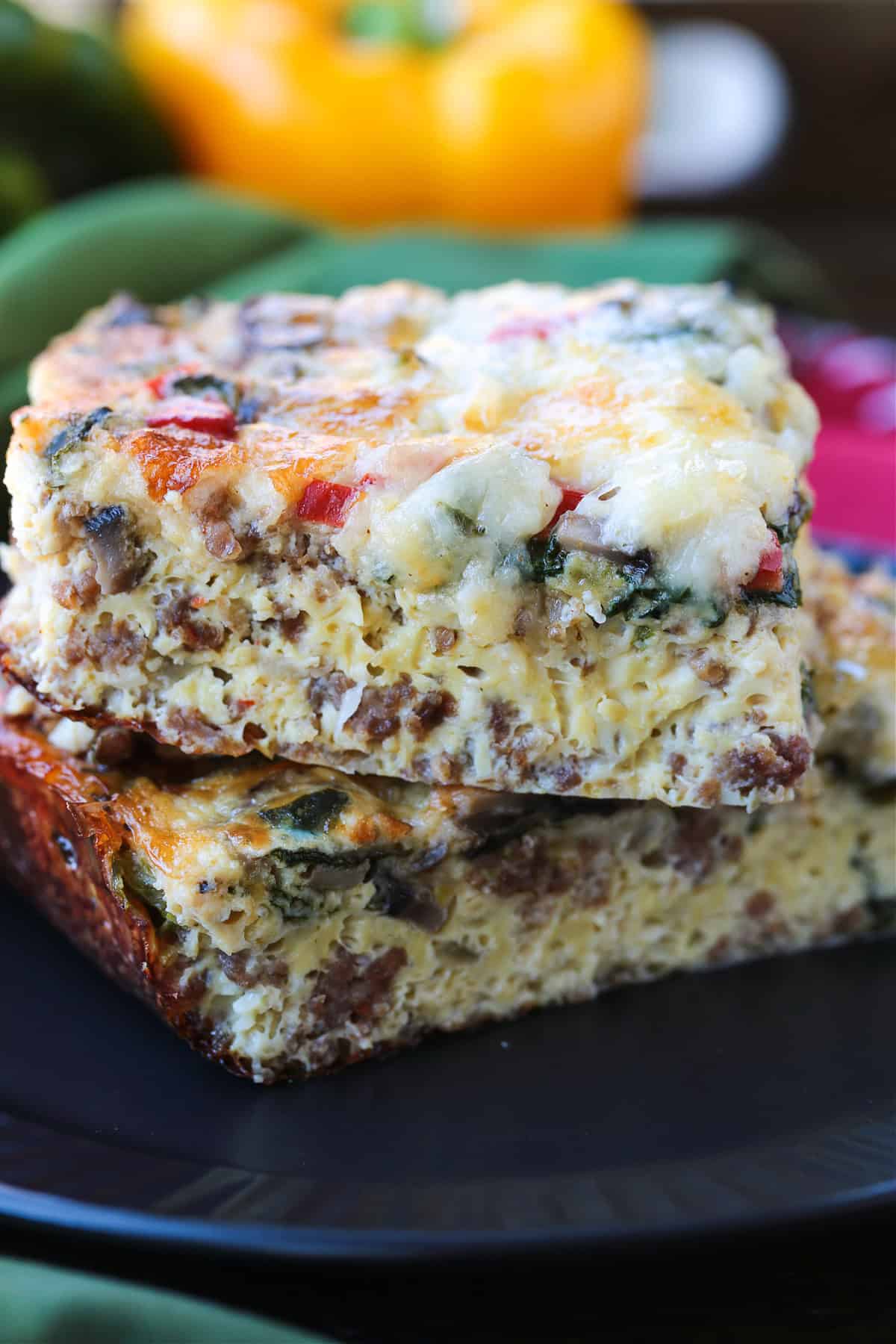 This Italian Breakfast Casserole is delicious for brunch or dinner with a salad! We love this cozy and hearty casserole any time of the day! slices of egg casserole with sausage stacked on black plate
