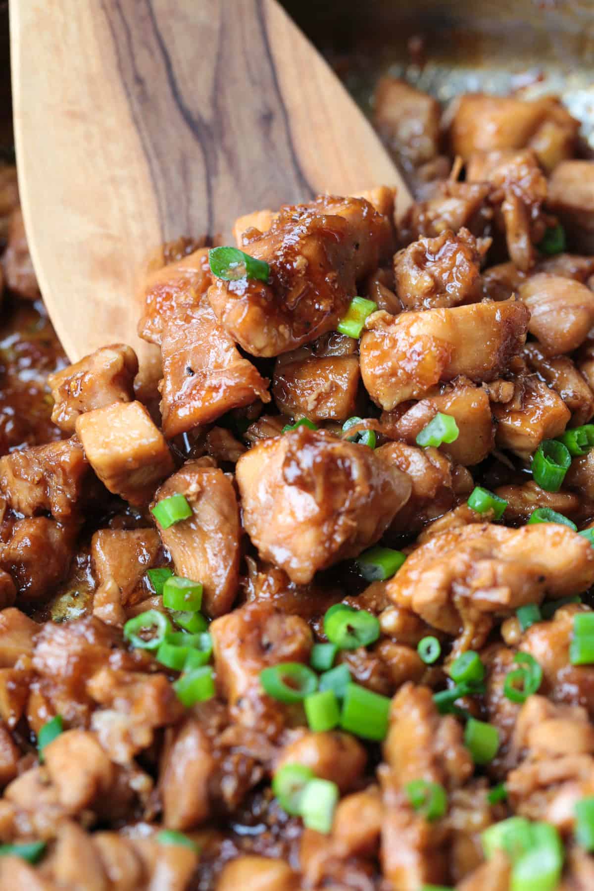 Our Easy Bourbon Chicken is a family favorite dinner recipe! Tender chicken in a sweet and tangy sauce with just a splash of bourbon. close up of bourbon chicken with wooden spatula
