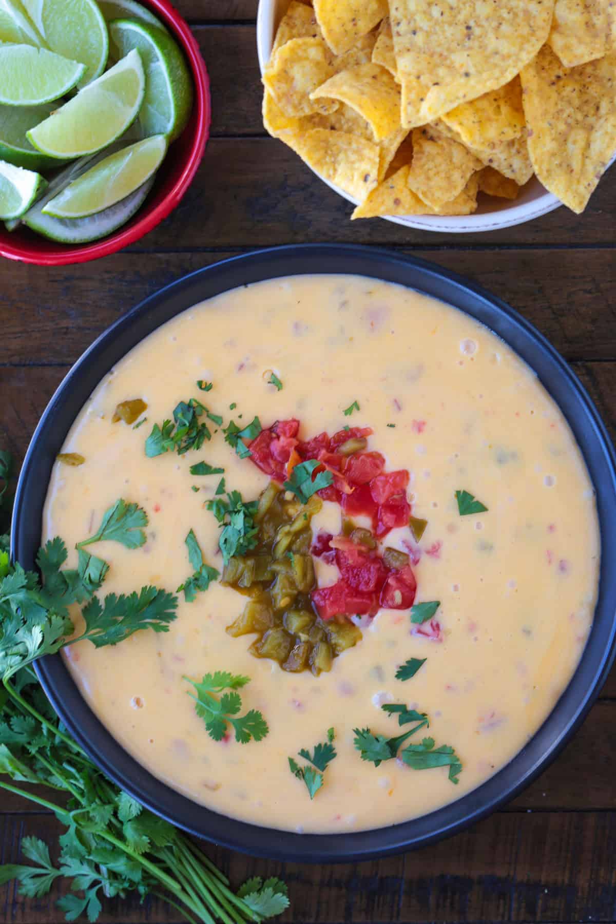 Slow Cooker Queso is going to be the center of attention at any party or game day! Use it as a dip, drizzle on nachos or use in burritos! bowl of cheese queso dip with limes and chips on the side