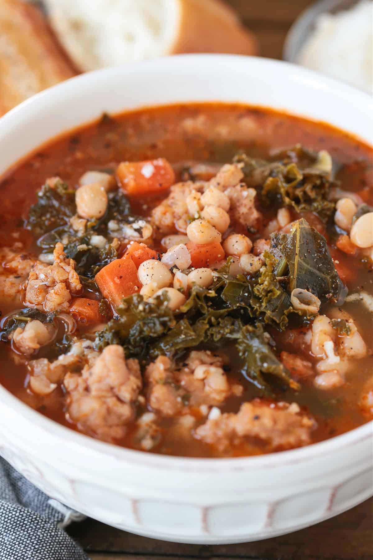Flavorful White Bean and Sausage Soup is so hearty and nourishing. Tender white beans, kale and chicken sausage with a touch if white wine. soup with white beans and sausage in a white bowl with bread