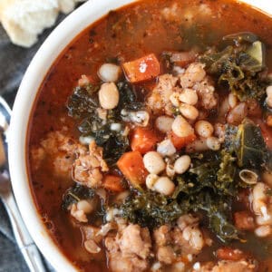 soup with sausage, kale and beans in a bowl with bread on the side