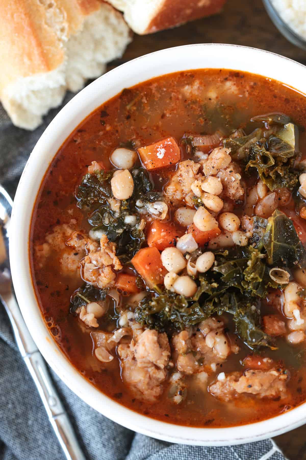 Flavorful White Bean and Sausage Soup is so hearty and nourishing. Tender white beans, kale and chicken sausage with a touch if white wine. soup with sausage, kale and beans in a bowl with bread on the side