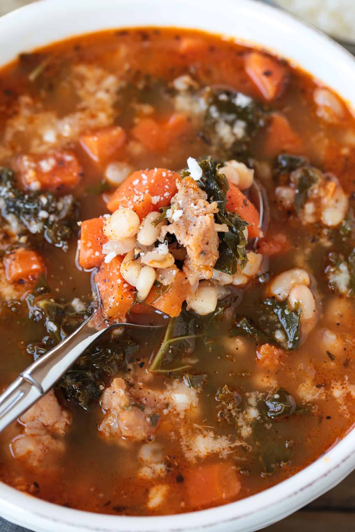 Flavorful White Bean and Sausage Soup is so hearty and nourishing. Tender white beans, kale and chicken sausage with a touch if white wine. soup with vegetables and sausage on a spoon in a bowl