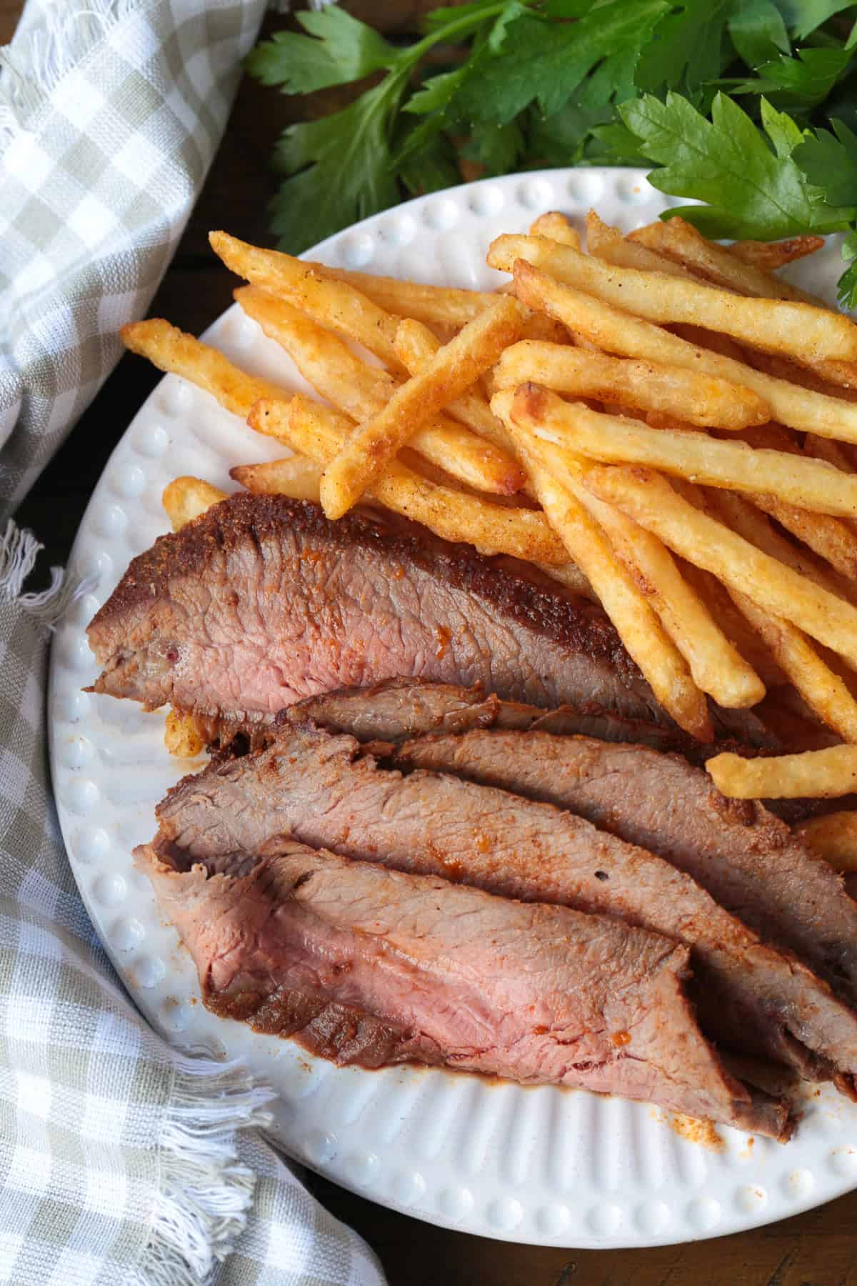 Need dinner fast? Our Air Fryer Flank Steak recipe delivers a tender, juicy, and flavorful steak with a crispy sear in just minutes! sliced steak on a plate with french fries