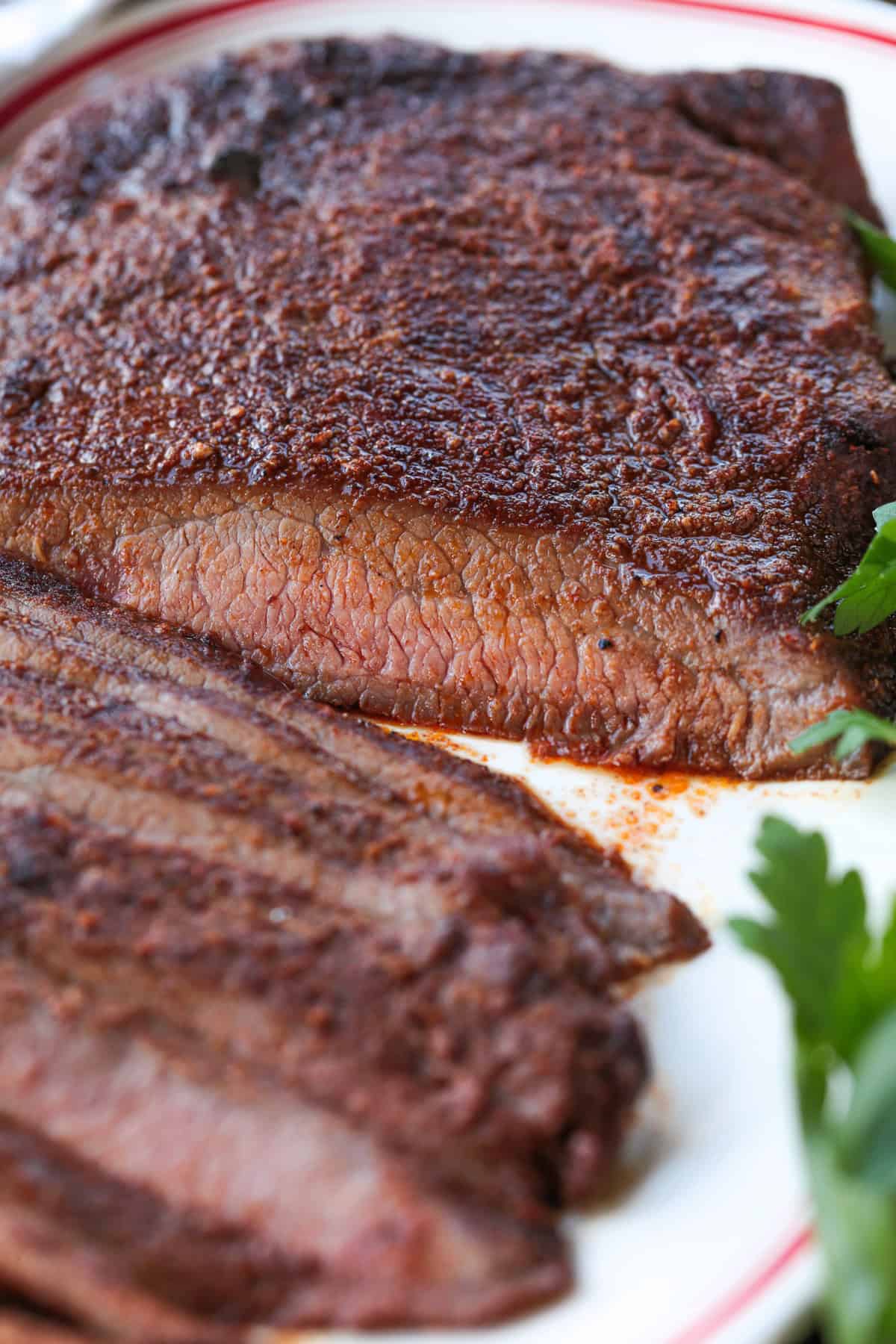 Need dinner fast? Our Air Fryer Flank Steak recipe delivers a tender, juicy, and flavorful steak with a crispy sear in just minutes! close up of sliced flank steak on platter