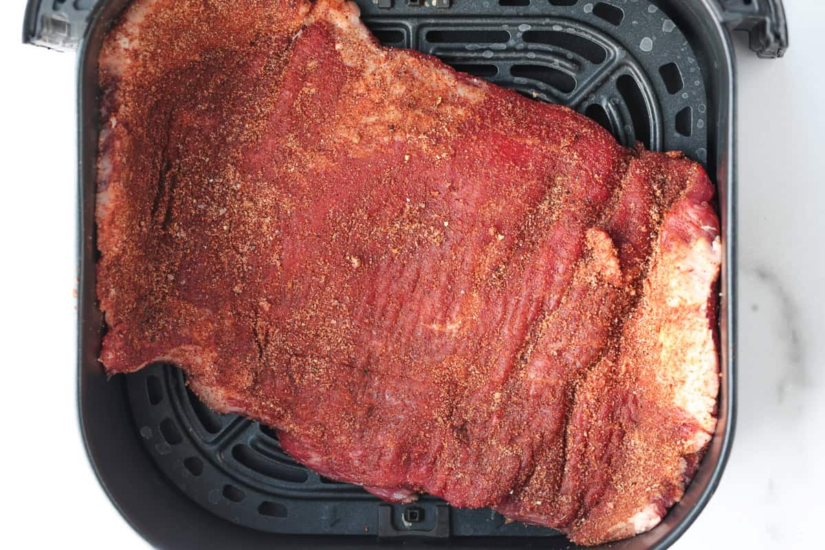 Need dinner fast? Our Air Fryer Flank Steak recipe delivers a tender, juicy, and flavorful steak with a crispy sear in just minutes! seasoned flank steak in air fryer basket