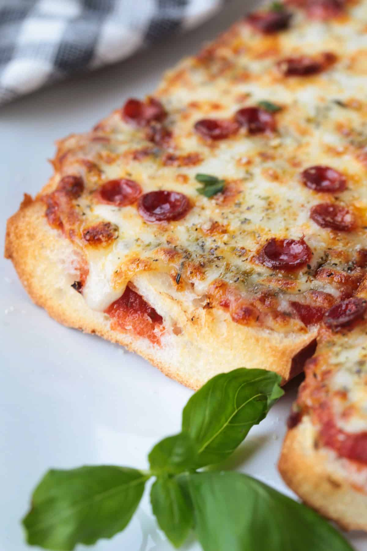 This Air Fryer French Bread Pizza is crispy, cheesy perfection! Ready in minutes, it’s an easy weeknight dinner, quick lunch or snack. cut french bread pizza close up on plate