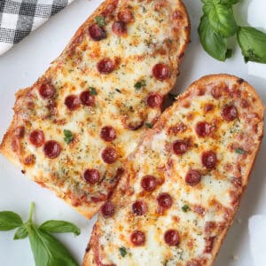 french bread pizzas with pepperoni on platter with basil