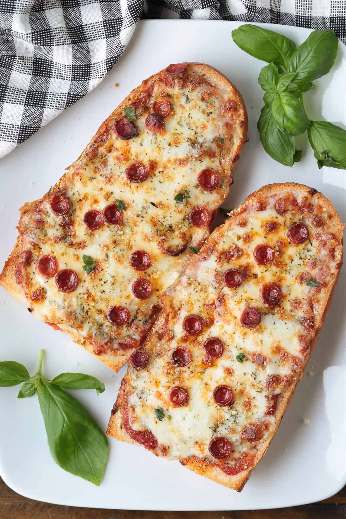 This Air Fryer French Bread Pizza is crispy, cheesy perfection! Ready in minutes, it’s an easy weeknight dinner, quick lunch or snack. french bread pizzas with pepperoni on platter with basil