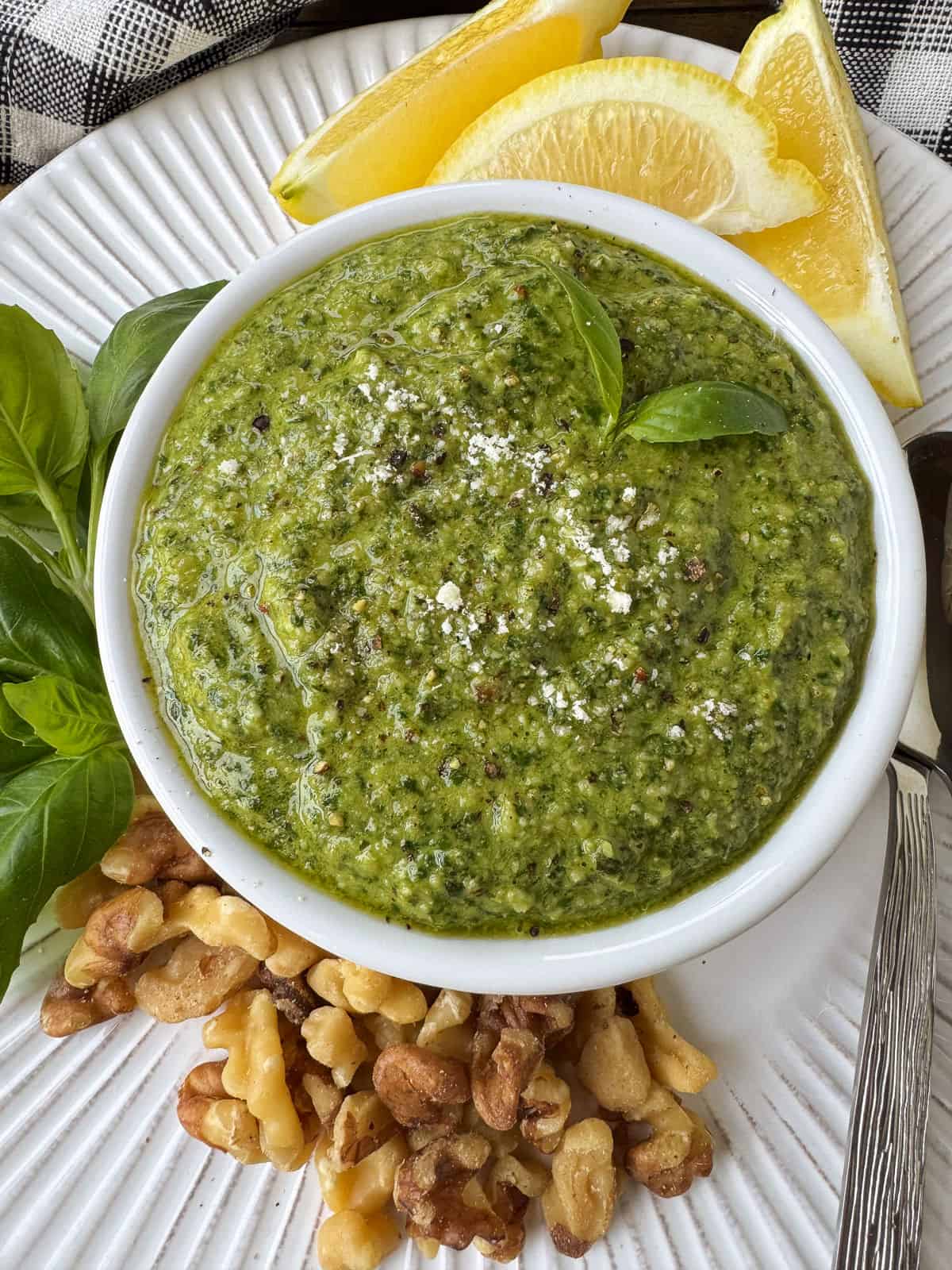 Make this tasty basil walnut pesto with just a few simple ingredients. A quick, vibrant sauce for chicken, fish or steak and so much more! basil pesto with walnuts in bowl with lemons on the side