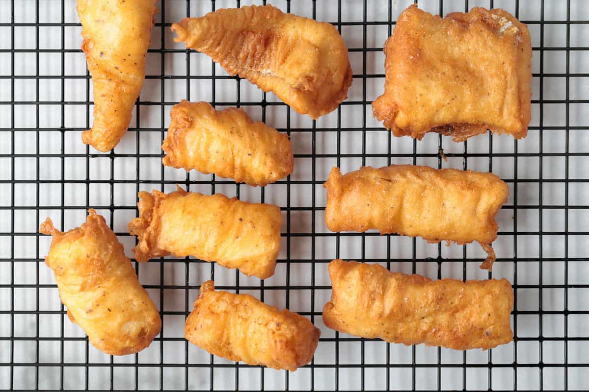 Make crispy, golden beer battered cod at home with our easy recipe! Flaky cod coated in a light beer batter and fried to a crispy perfection. fried cod pieces on wire rack