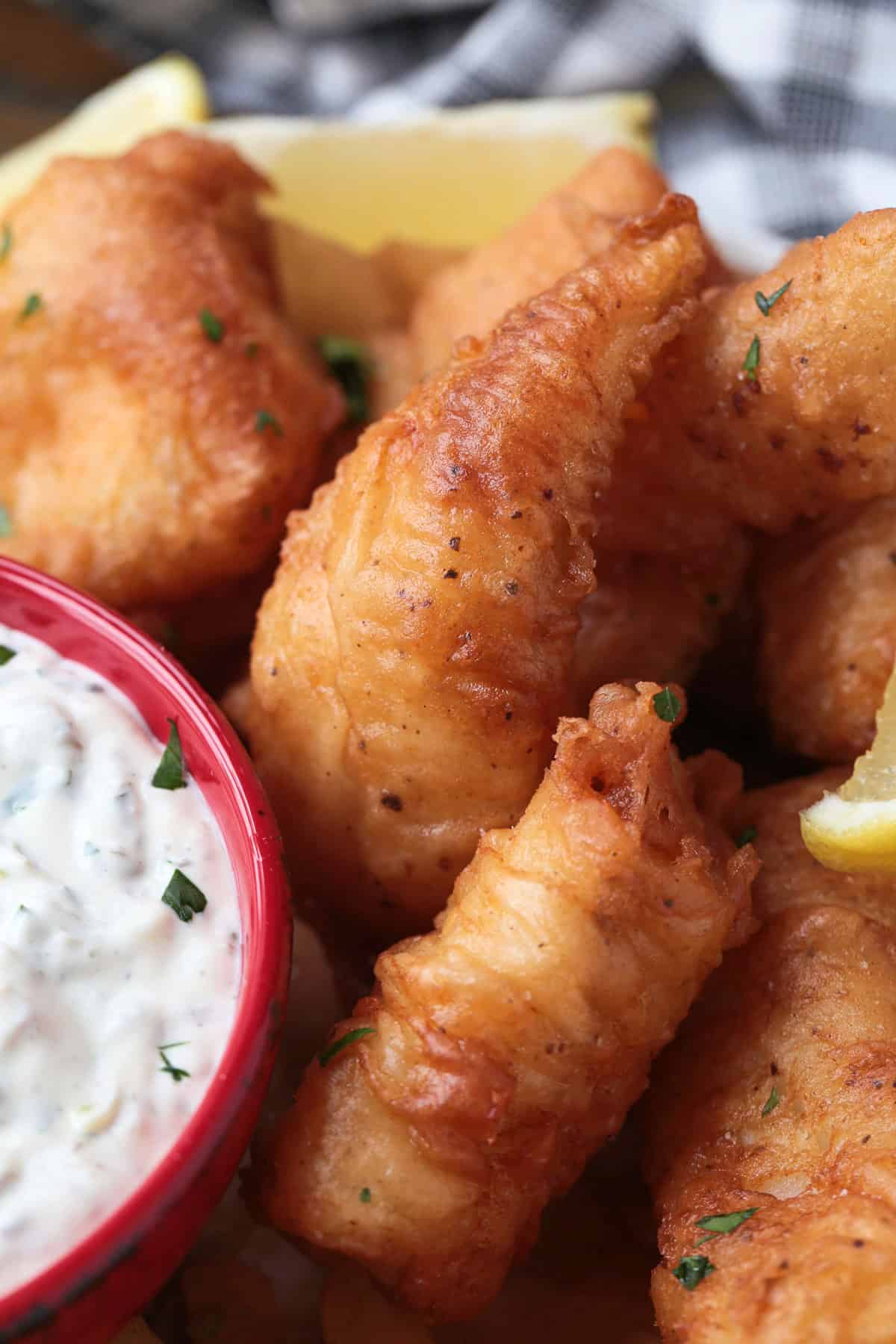Make crispy, golden beer battered cod at home with our easy recipe! Flaky cod coated in a light beer batter and fried to a crispy perfection. fried cod on platter with sauce and lemons