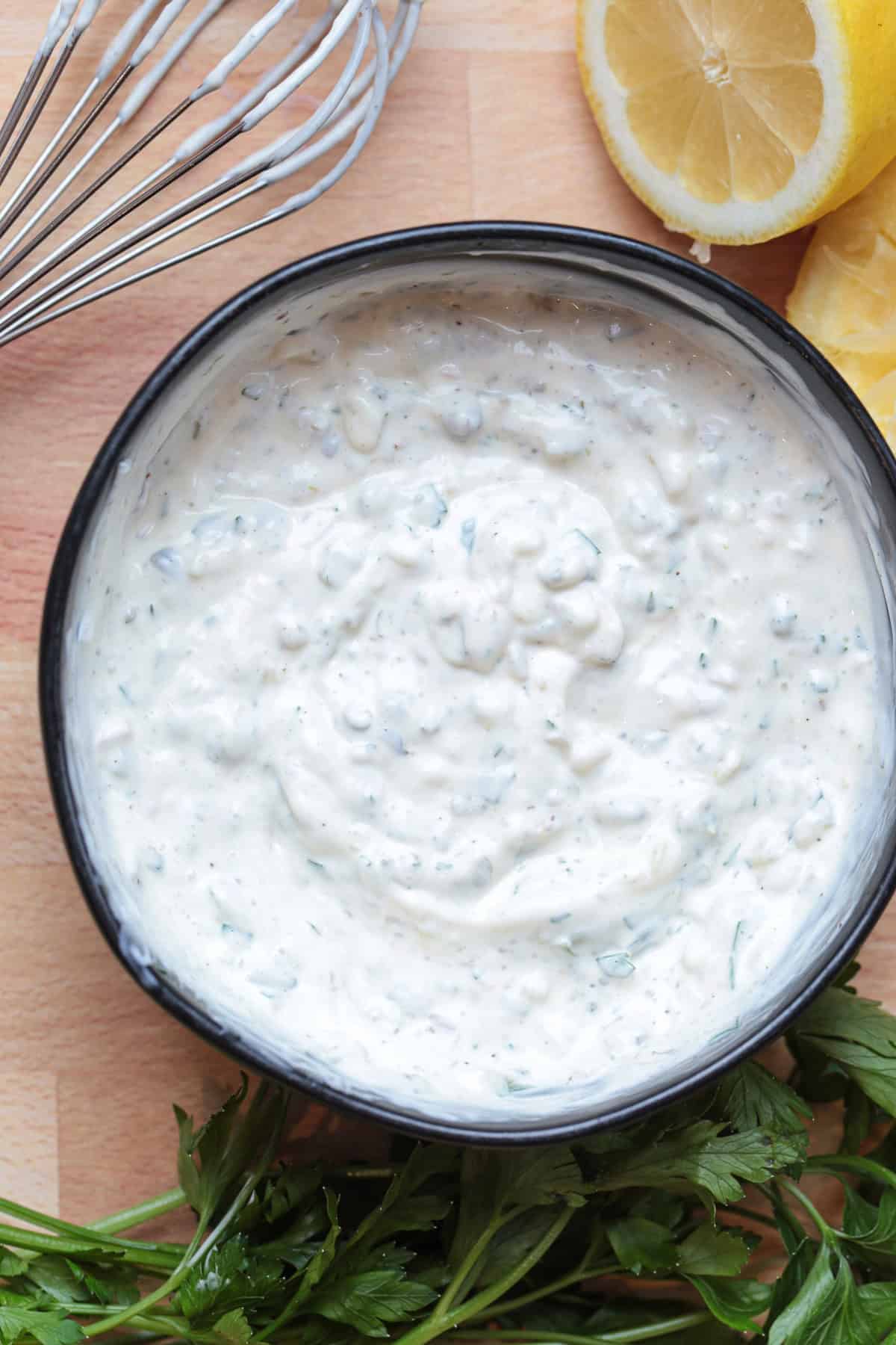 Easy homemade tartar sauce is creamy, tangy, and packed with fresh flavor. Delicious on fish, shrimp, fries, and so munch more! tartar sauce in a black bowl with whisk and lemon on the side