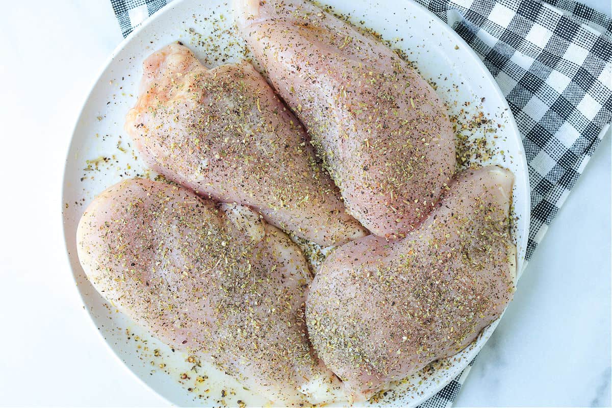 Grilled Chicken Margherita is an easy dinner recipe made with juicy grilled chicken, fresh mozzarella, ripe tomatoes, garlic, and pesto. chicken breasts on a plate with seasoning