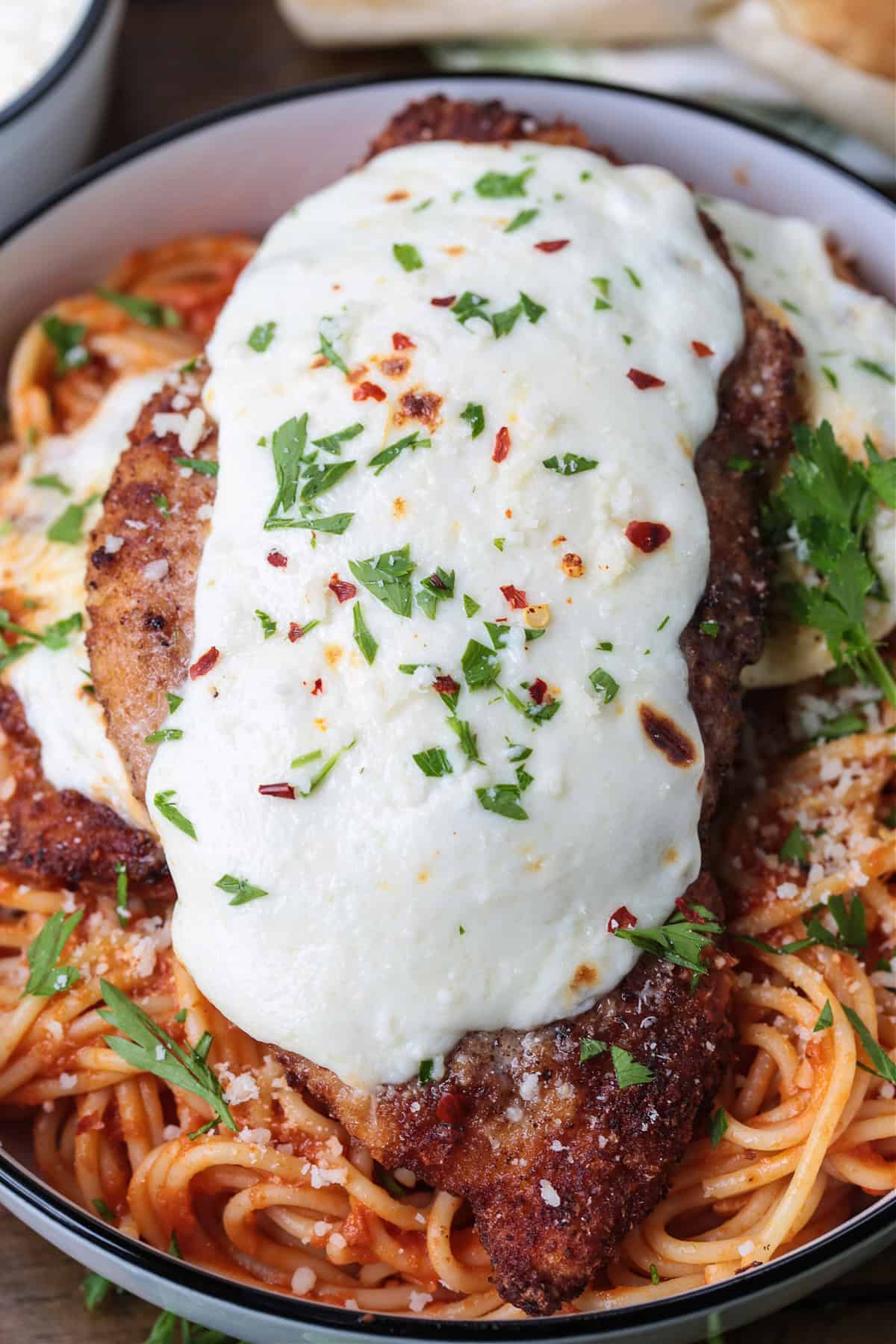 Super crispy chicken parmesan, not made soggy form baking in sauce. Serve over pasta or on a plate with marinara for the ultimate crispiness! close up of chicken parmesan on a bed of spaghetti