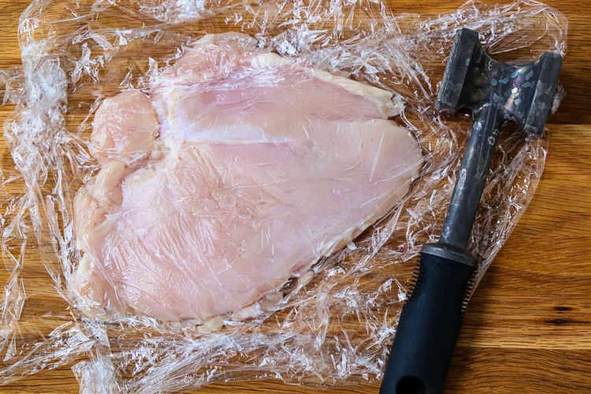 Super crispy chicken parmesan, not made soggy form baking in sauce. Serve over pasta or on a plate with marinara for the ultimate crispiness! chicken breast with plastic wrap on top and meat tenderizer on the side