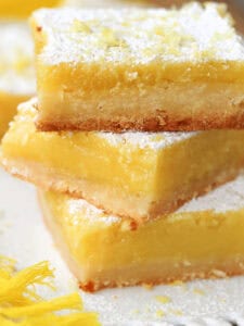 large lemon bars stacked on plate with sugar