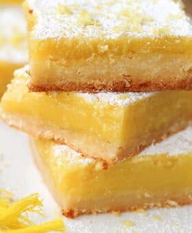 large lemon bars stacked on plate with sugar