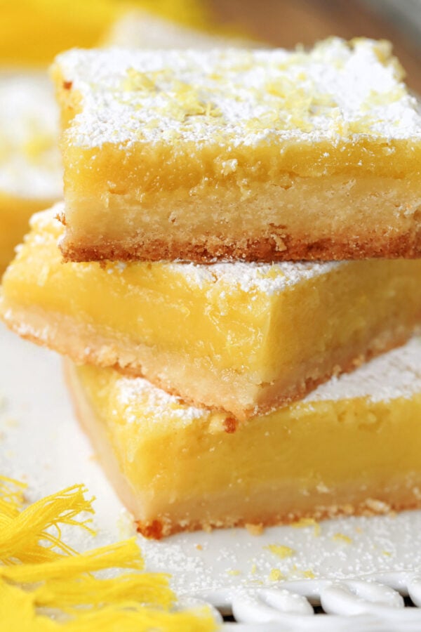 large lemon bars stacked on plate with sugar