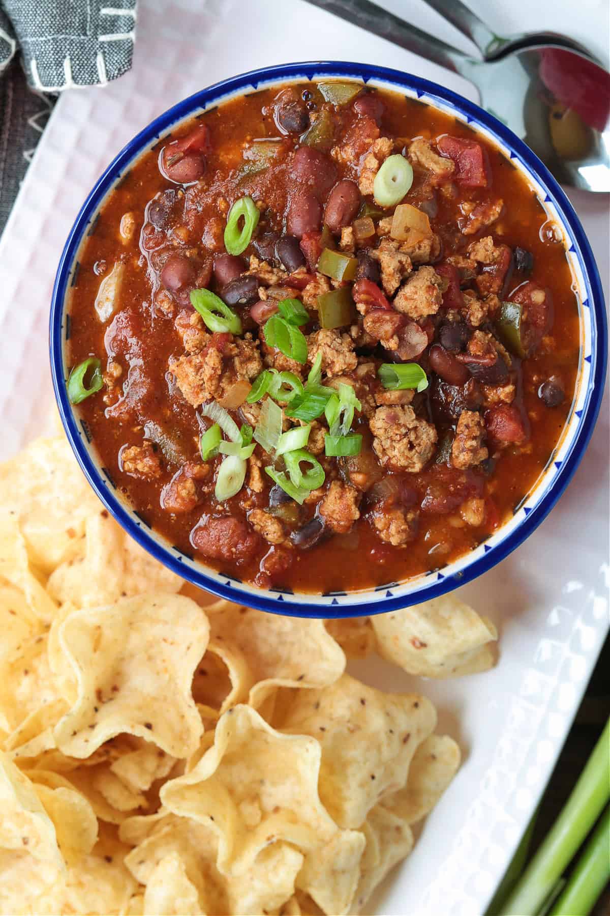This slow cooker turkey chili is packed with lean ground turkey, vegetables and vibrant spices. Perfect for easy dinners or game days! turkey chili in a bowl topped with scallions and a side of chips