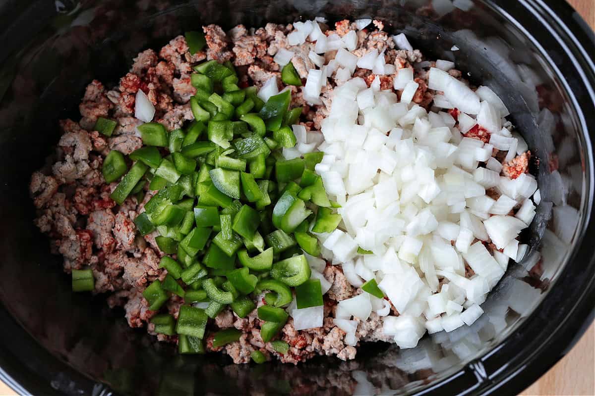 This slow cooker turkey chili is packed with lean ground turkey, vegetables and vibrant spices. Perfect for easy dinners or game days! diced green peppers and onions in slow cooker with ground turkey