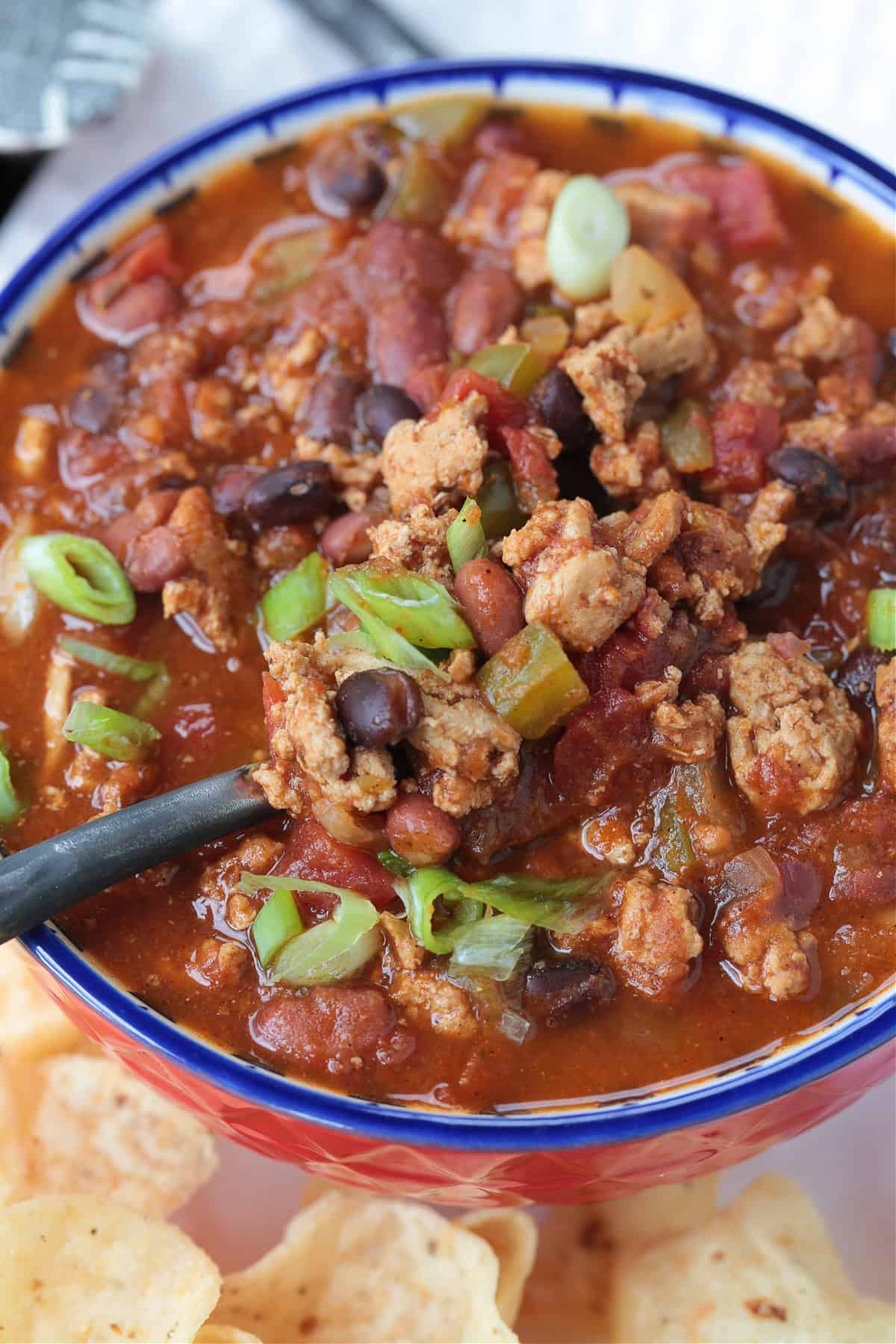 This slow cooker turkey chili is packed with lean ground turkey, vegetables and vibrant spices. Perfect for easy dinners or game days! turkey chili in a bowl with a spoon
