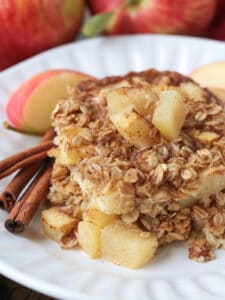 baked oatmeal on a white plate with apples and cinnamon sticks