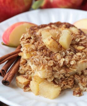 baked oatmeal on a white plate with apples and cinnamon sticks