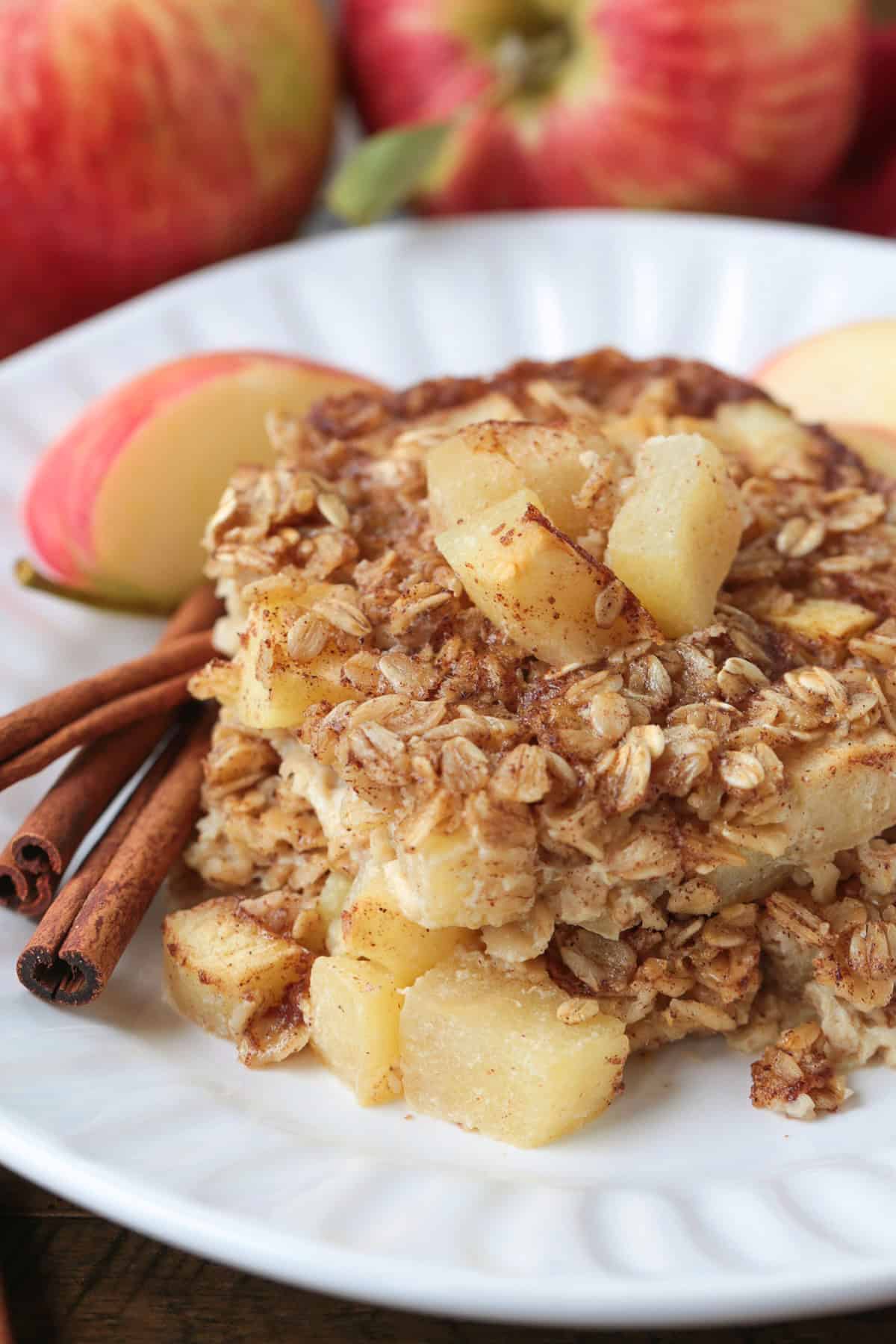 baked oatmeal on a white plate with apples and cinnamon sticks