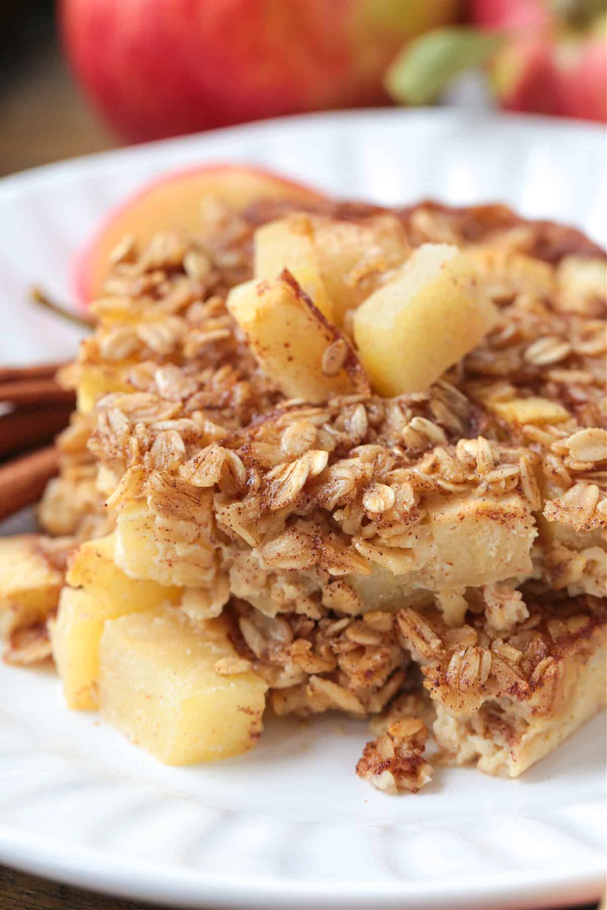 squares of baked apple oatmeal on plate with cinnamon sticks and apples