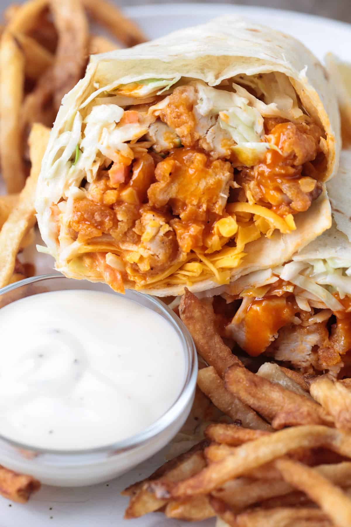 buffalo chicken wrap cut in half and stacked on a plate with sauce and fries