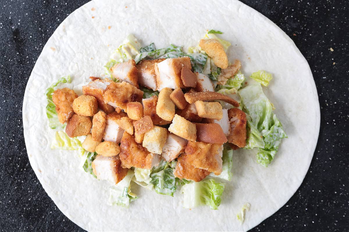 This Chicken Caesar Wrap made with our homemade Caesar dressing is the ultimate quick meal. A tasty lunch or dinner that's ready in minutes! chicken, lettuce and croutons on a tortilla
