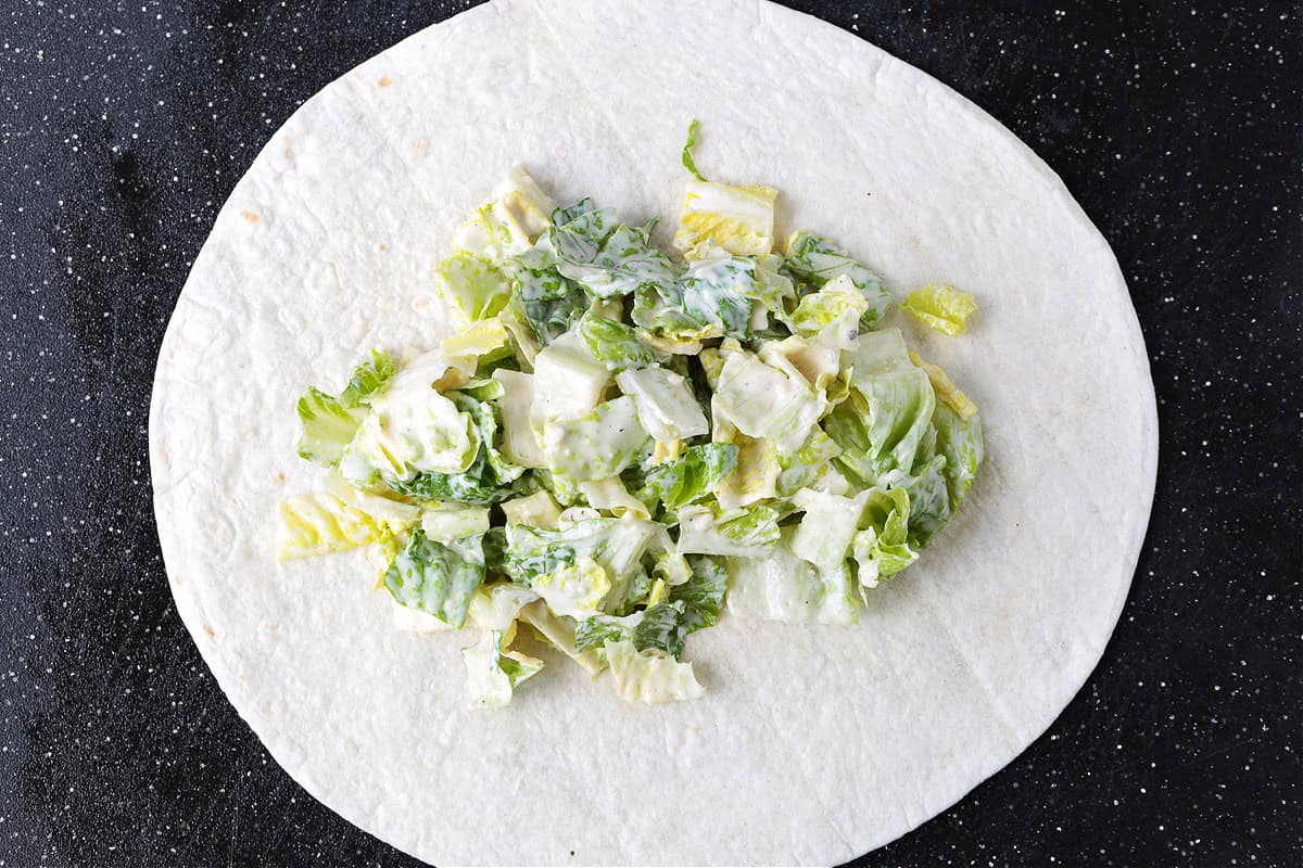 This Chicken Caesar Wrap made with our homemade Caesar dressing is the ultimate quick meal. A tasty lunch or dinner that's ready in minutes! shredded lettuce with caesar dressing on a tortilla