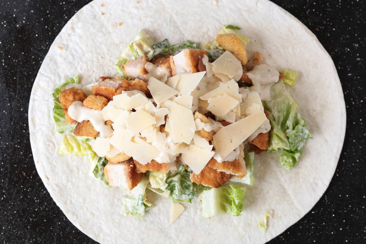 This Chicken Caesar Wrap made with our homemade Caesar dressing is the ultimate quick meal. A tasty lunch or dinner that's ready in minutes! shaved parmesan cheese with chicken, lettuce and croutons on tortilla