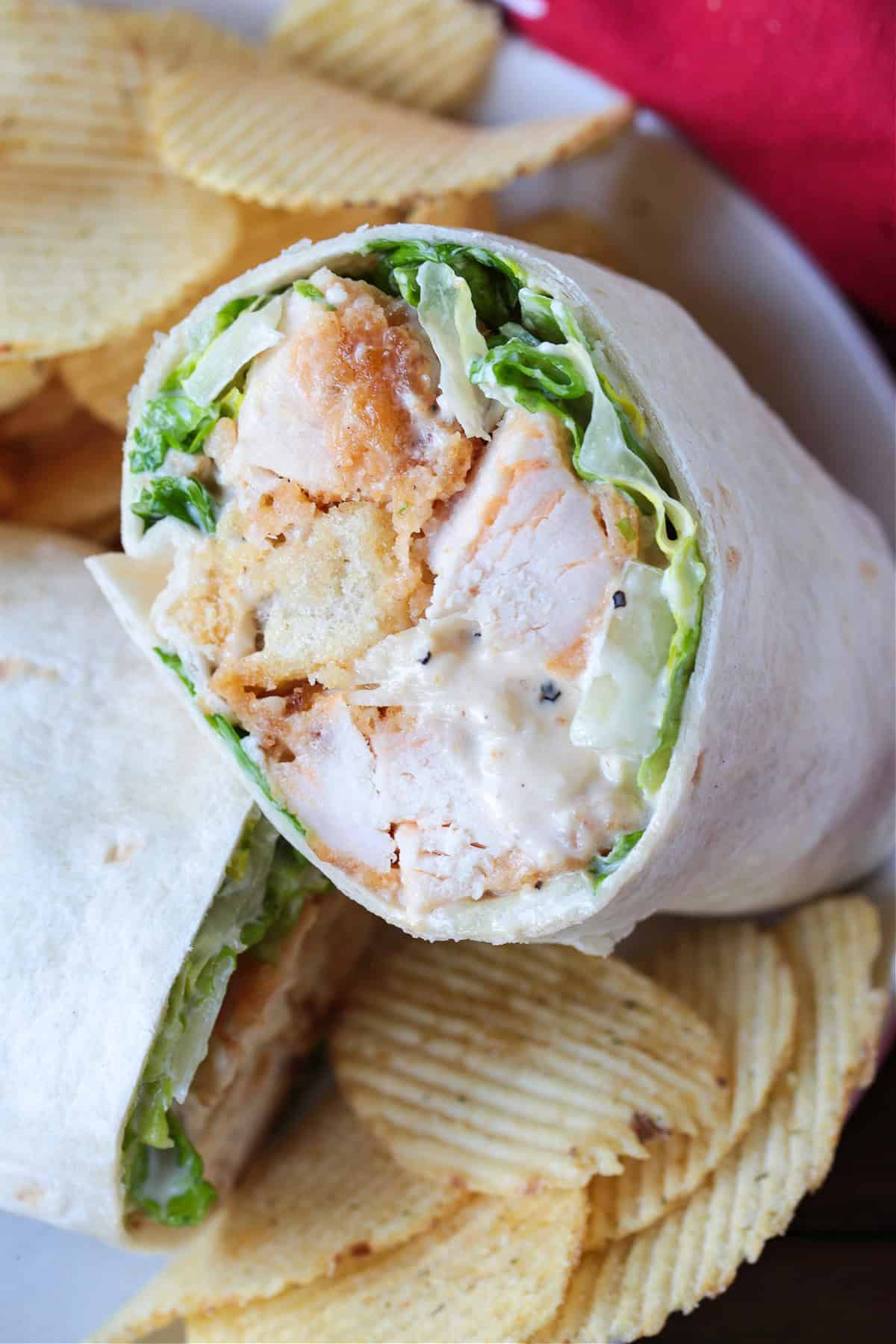 This Chicken Caesar Wrap made with our homemade Caesar dressing is the ultimate quick meal. A tasty lunch or dinner that's ready in minutes! chicken wrap with lettuce and croutons cut in half on a plate with chips