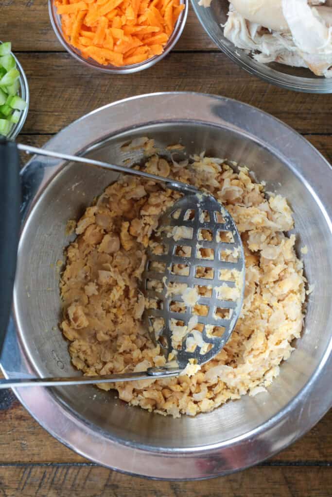 Chickpea Chicken Salad is made with tender chicken, crunchy veggies and buttery chickpeas. A protein packed meal that's ready in minutes! bowl with mashed chickpeas and potato masher