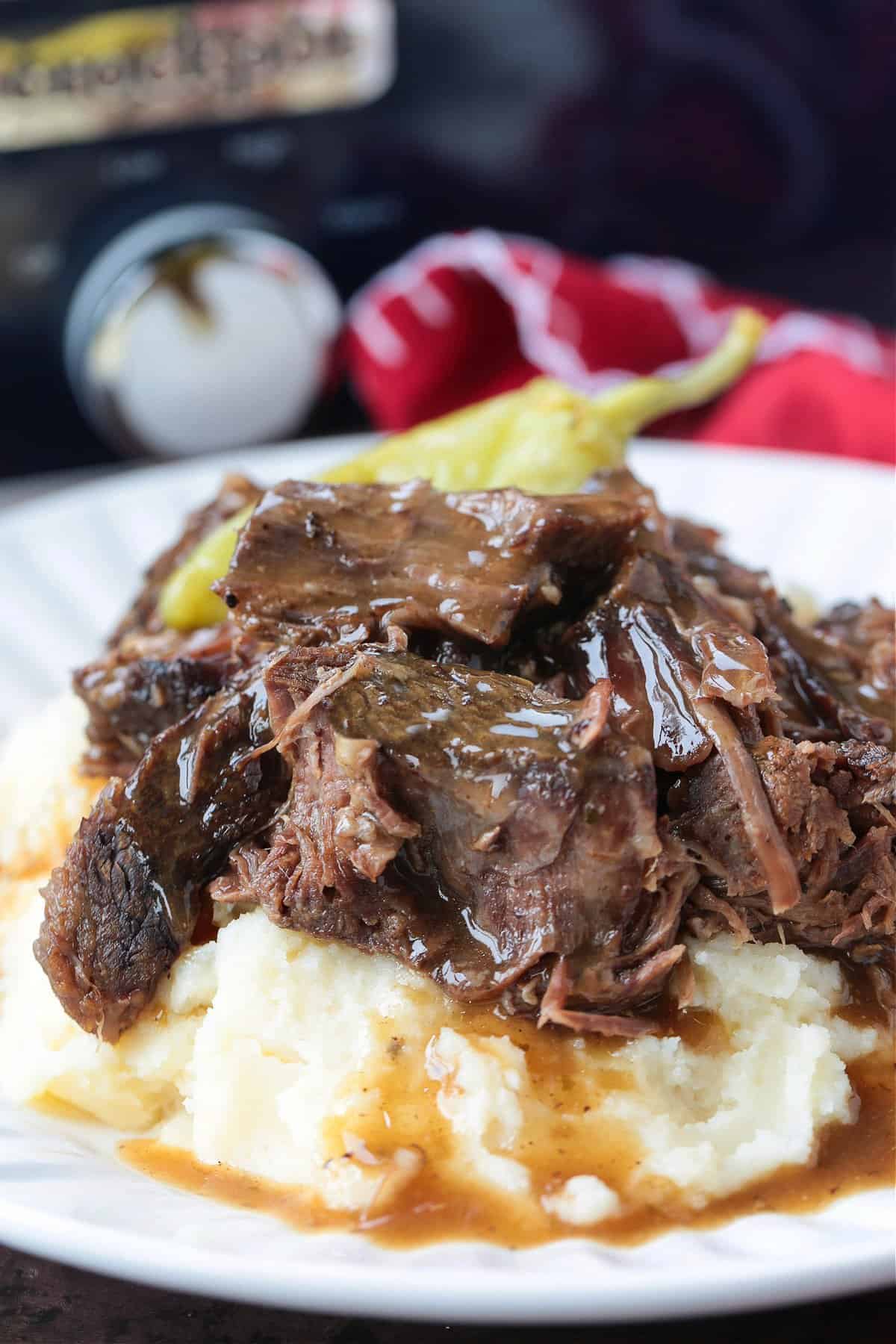 Slow Cooker Mississippi Pot Roast is tender and delicious in a tangy brown gravy. An easy crock pot dinner the whole family will love! shredded pot roast with pepperoncini peppers on mashed potatoes